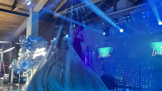 Quinceañera bailando el vals sobre una pista LED con pantallas laterales proyectando su nombre