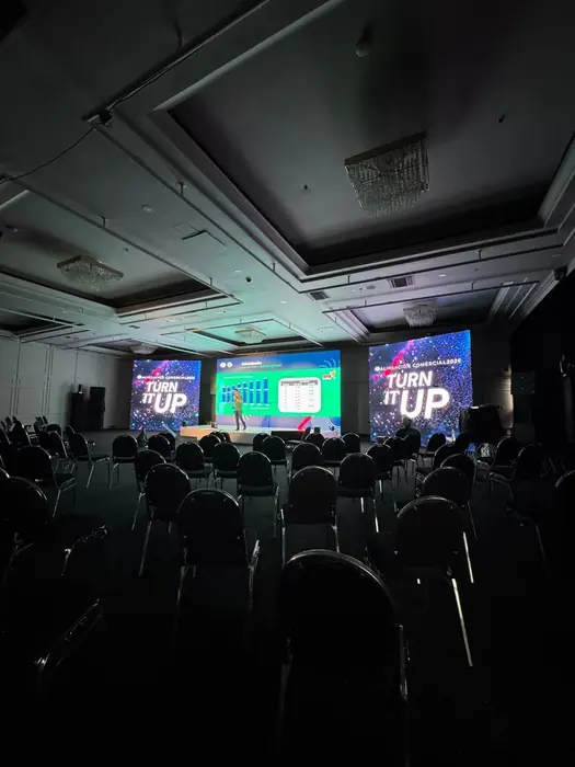 Sala de convenciones con tres pantallas LED y asistentes sentados frente al escenario