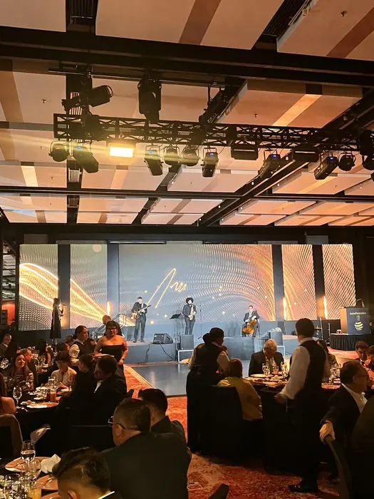 Invitados en las mesas de un salón de gala con una pantalla LED iluminando el fondo